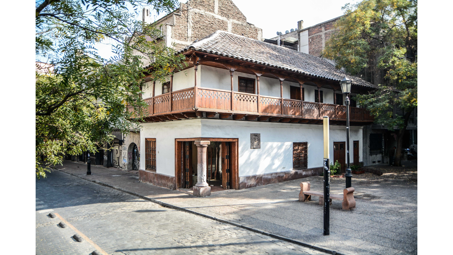 Facha de la Posada del Corregidor desde calle Esmeralda, en donde se aprecian los dos niveles, destaca pilar de piedra, balcón volado en madera techo de tejas. se aprecia la plaza del corregidor que rodea su entorno