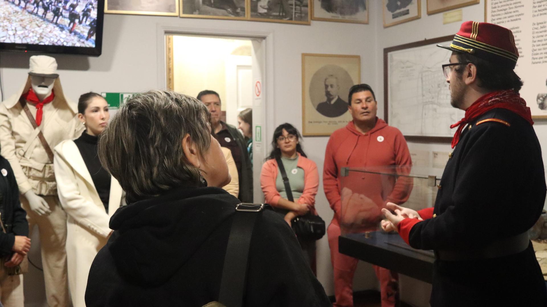 La fotografía muestra el hall central de nuestro museo con público escuchando la charla de un voluntario vestido con uniforme de soldado chileno de la guerra del pacífico