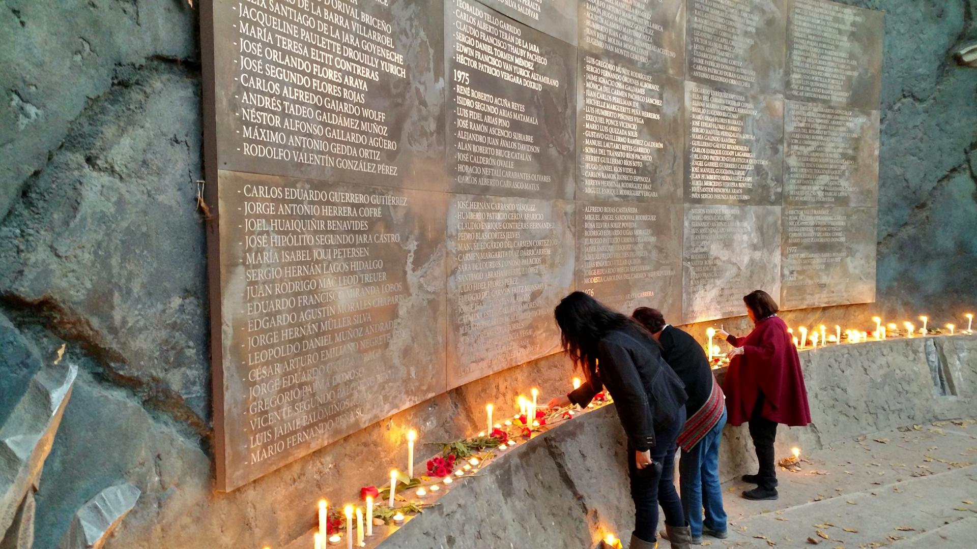 Personas conmemorando a detenidos desaparecidos y ejecutados políticos en el muro de los nombres