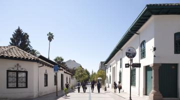 dos casas coloniales de color blanco con tejas de greda, ubicada una frente a la otra y separadas por un paseo petaonal donde transita gente.