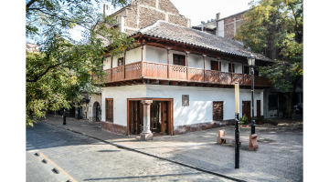 Facha de la Posada del Corregidor desde calle Esmeralda, en donde se aprecian los dos niveles, destaca pilar de piedra, balcón volado en madera techo de tejas. se aprecia la plaza del corregidor que rodea su entorno